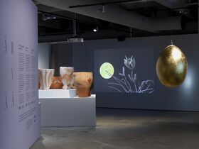 Art exhibition with pottery, a large golden egg, and a projection of flowers and a moon on the wall.