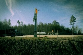 A Shell petrol station with a truck parked nearby, surrounded by trees under a blue sky.