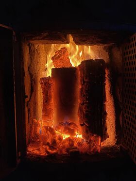 A close-up of burning logs inside a fireplace, with bright flames and glowing embers.