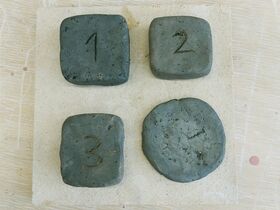 Four grey stones on a beige surface, numbered 1 to 4. Three stones are square, one is round.