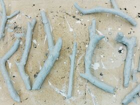 Grey sticks arranged on a beige surface with white paint splatters.