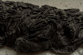 Close-up of a crumpled, dark fabric with intricate folds and wrinkles on a light surface.