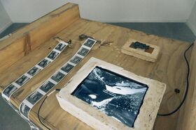 A wooden table with a stone frame displaying a black and white image, and film strips laid out beside it.