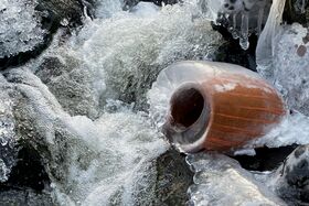 A frozen stream with an icy brown pot partially submerged in the water.