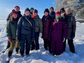 A group of people in winter clothing standing on snow with trees in the background.