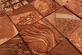 A collection of textured, brown ceramic tiles with various patterns and designs, including swirls, lines, and floral motifs.