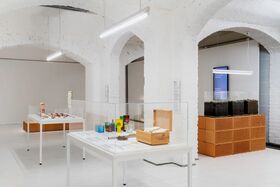 A modern exhibition room with white walls and arches, displaying various items in glass cases and on tables.
