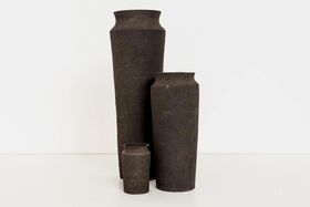 Three dark brown ceramic vases of different heights placed on a white surface.