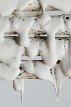 Close-up of white, creamy substance dripping over textured, speckled surface.