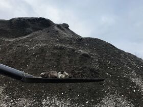 A shovel with soil and rocks in front of a large mound of dirt under a cloudy sky.