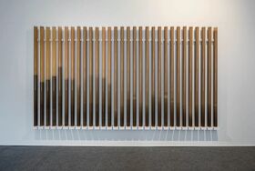 A wall-mounted installation of vertical tubes filled with varying levels of brown liquid.