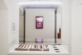 A museum exhibit with a glass case displaying various items and a digital screen on the wall showing text.