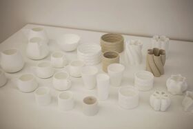 A collection of white and beige ceramic cups, bowls, and vases on a white surface.