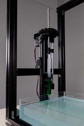 A machine with a syringe injecting green liquid into a clear tank filled with water.