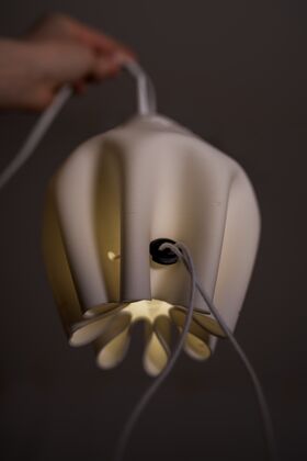 A hand holding a white, modern pendant lamp with a unique, curved design and visible cord.