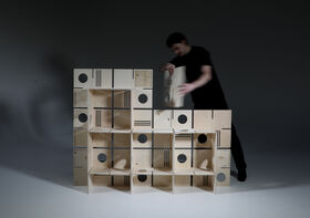 A person arranges modular wooden shelves with circular and linear cutouts in a staggered formation.