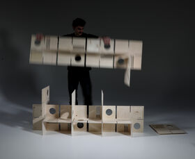 A person assembling wooden panels with circular and rectangular cutouts on a white surface.