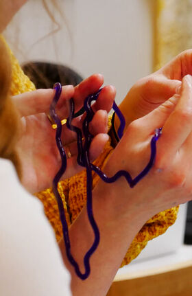 Two hands holding a flexible, purple object. The person wears a yellow knitted garment.