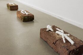 Three bricks with white coral-like sculptures on a grey floor near a white wall.