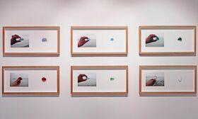 Six framed photos of hands holding coloured stones against a grey background, arranged in two rows on a white wall.