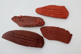 Four pieces of reddish clay with text imprints about soil on a white background.