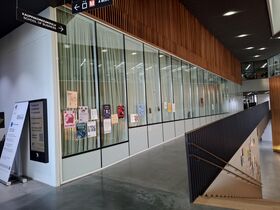 Modern hallway, glass wall with posters and stairs descending on the right