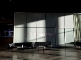 Lobby with black sofas, round tables and papers on tall frosted glass wall lit by sunlight