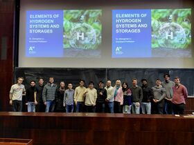 Opiskelijaryhmä luentosalissa kahden “Elements of Hydrogen Systems and Storages” -diaesityksen alla.