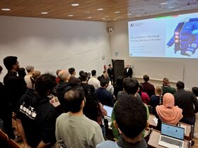 Students standing in a lecture hall as two speakers present slides on electrical heating bio-based textiles