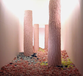 Tall tree-like columns in an illuminated room with countless colourful cups scattered on the floor.