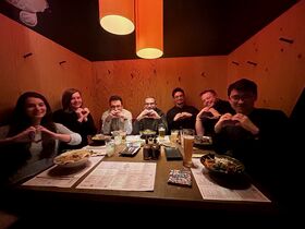 Ryhmä ravintolapöydässä ruoan ja juomien äärellä, kaikki tekevät käsillään sydämen