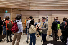 People engaging in discussions and having coffee in a wooden panelled room with posters on the walls.