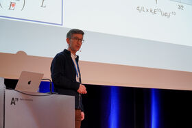 Person standing in front of a projection screen. A laptop is placed on a podium with Aalto University logo.