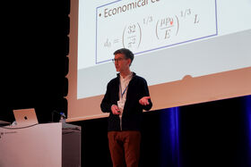 A person giving a presentation with mathematical formulas projected on a screen, standing next to a podium with a laptop.