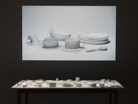 A projected image of white earthenware. Below, an assortment of similar ceramics is displayed on a table.