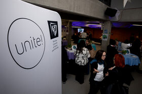 People at a university event indoors. A poster reads 'unite!' with 'Wroclaw University of Science and Technology' beneath.