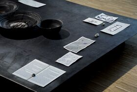 Art display with grey bowls and scattered drawings on a dark low platform over a wooden floor