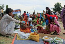 Outdoor village market with people in colourful clothes selling vegetables, chillies and grains on the ground