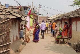 Narrow village lane with people in colourful clothes outside clay and brick houses on a sunny day