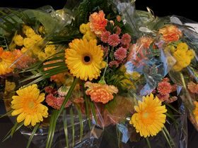 Kimpullinen keltaisia ja oransseja kukkia vihreine lehtineen, käärittynä kirkkaaseen muoviin