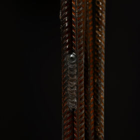 Close-up of rusty ribbed steel rods welded together against a dark background