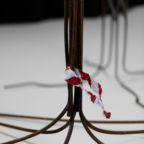 Rusty metal rods curve on a pale floor, with crumpled red and white paper caught around one rod.