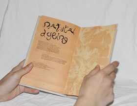 Hands holding an open orange booklet titled “Natural Dyeing” against a white fabric background
