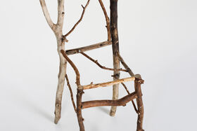 Artistic chair made of thin brown and pale wooden branches against a plain white background