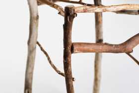 Close-up of a rustic stool made from intertwined light and dark brown tree branches.