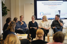 Panel of people discuss art education in a classroom, with a large presentation screen behind them.