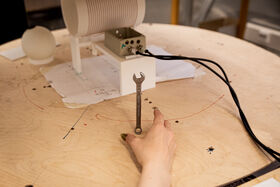 Hand holding upright spanner on cluttered wooden table with cables and a white electronic device