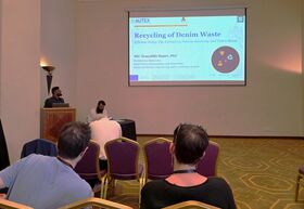 Conference room where a presenter shows a slide on recycling denim waste to seated attendees