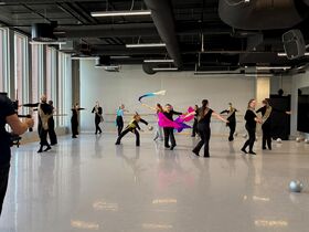Dancers in a bright studio twirl with colourful scarves and silver balls on the shiny floor