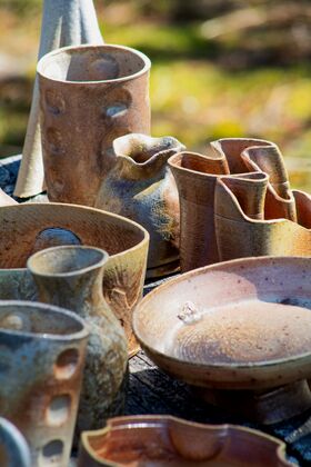 Assorted handmade brown and beige ceramic bowls and vases on an outdoor table in sunlight